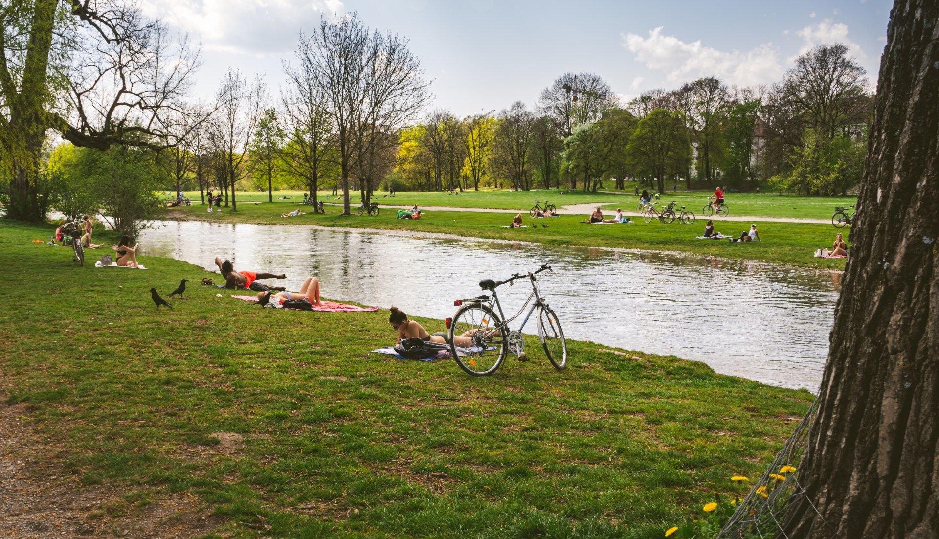 Personas descansando en el césped junto al agua en el Jardín Inglés de Múnich