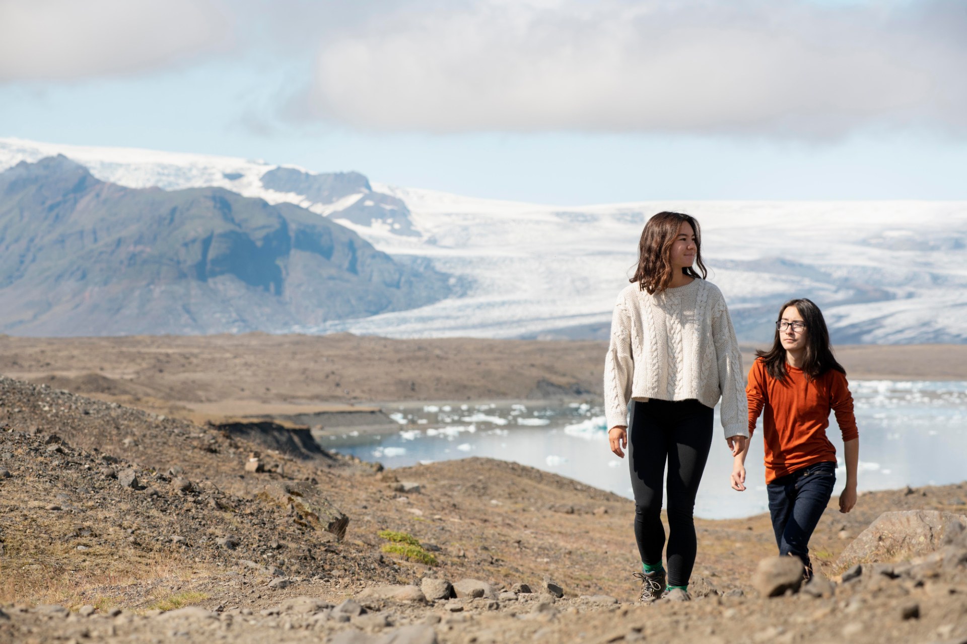 Dos jóvenes haciendo senderismo en Islandia con un glaciar y montañas al fondo