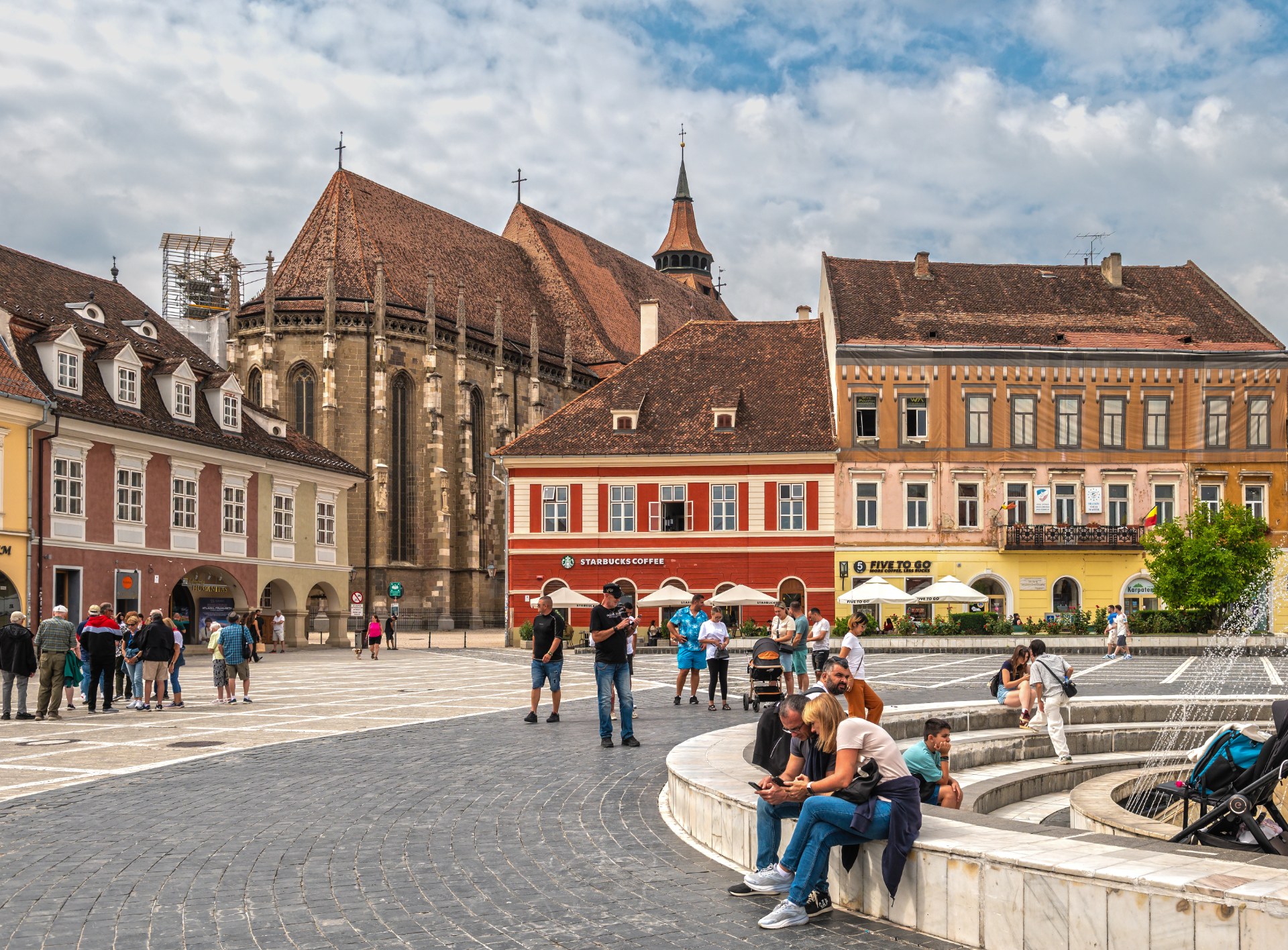 Jóvenes descansando junto a la fuente de la plaza del Consejo de Brasov, con la Iglesia Negra al fondo